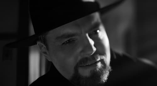 Orson Welles (Tom Burke) in black jacket and wide brimmed hat