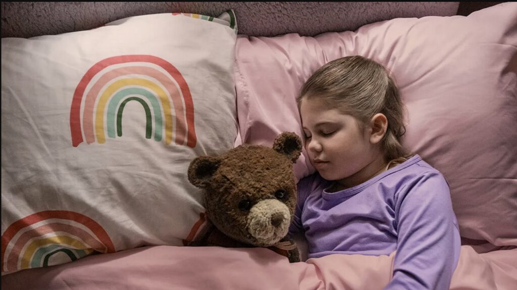A little girl snuggles her teddy bear in bed in Imaginary