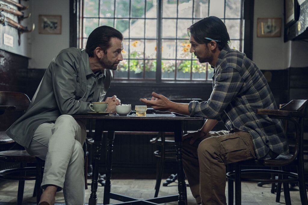 Ian Ventham and Bogden talk earnestly over a pub table in The Thursday Murder Club