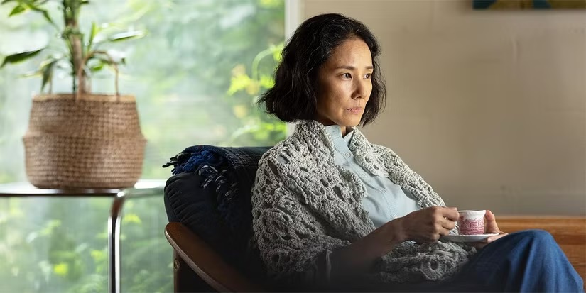 The older Etsuko (Yoh Yoshida) drinks a coffee in an armchair in A Pale View of Hills