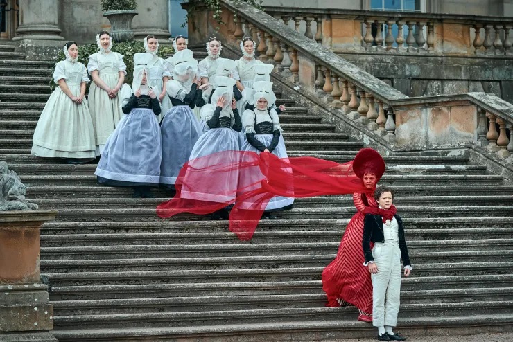 Maids watch on as Claire Frankenstein cuddles her son Victor at the bottom of their stately home stone steps in Guillermo del Toro's Frankenstein.
