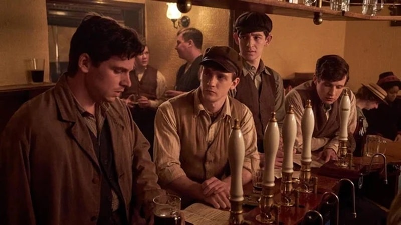 Clyde ( Jacob Dudman), Mitch (Shaun Thomas), Lofty (Oliver Briscombe) and Gilbert (Thomas Howes) stand at the bar in the film The Choral.