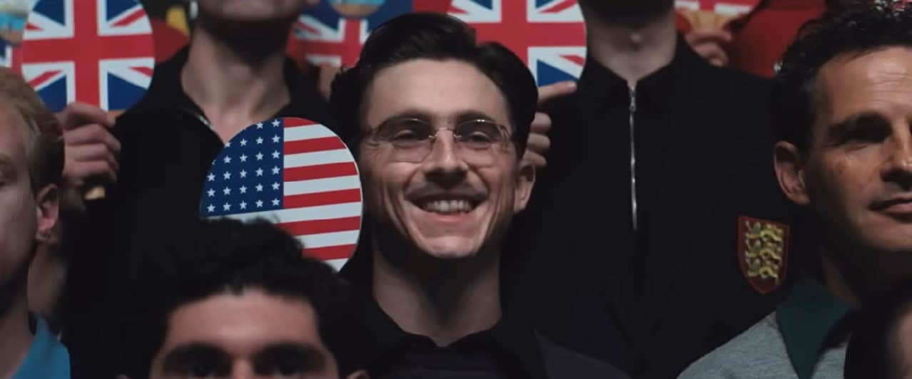 Marty Mauser (Timothée Chalamet) flashes a broad smile in what is supposed to be a serious photo in Marty Supreme