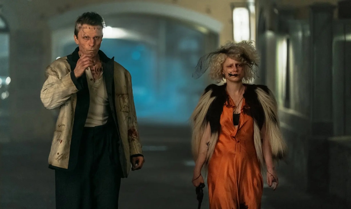 Frank (Christian Bale) and The Bride (Jessie Buckley) walking in a dimly lit street.