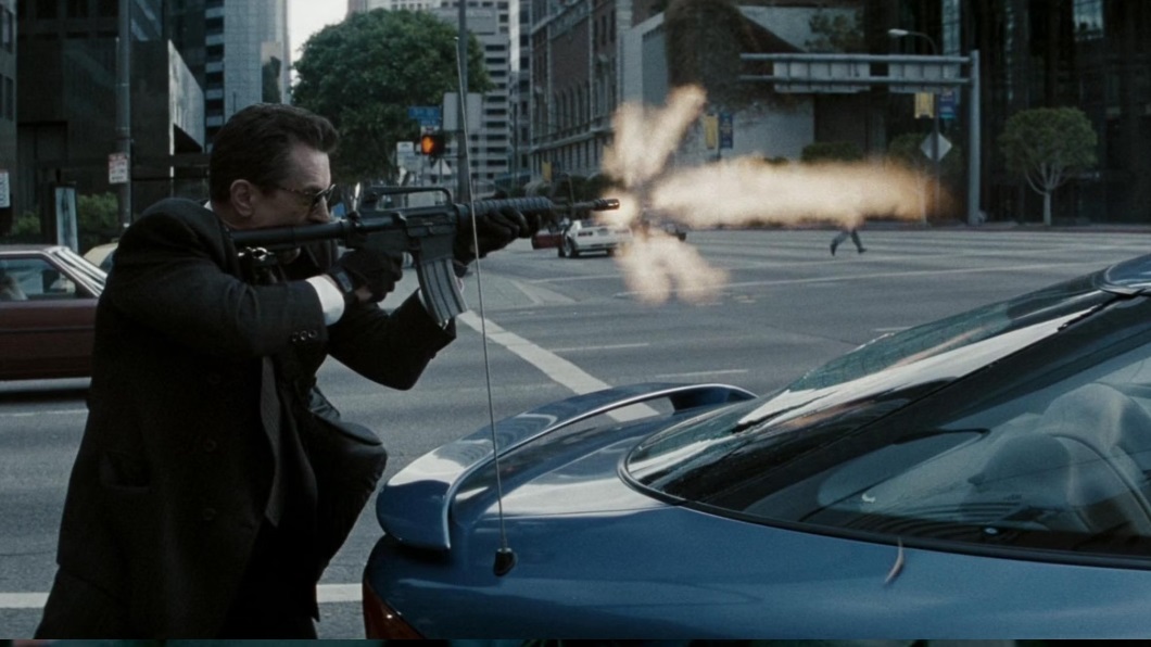 Neil McCauley (Robert De Niro) fires a heavy machine gun in the street in the movie Heat