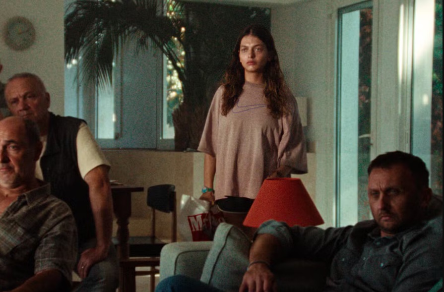 Lesia looks on concerned as the mafia gang in her father's house watch the TV news in The Kingdom.