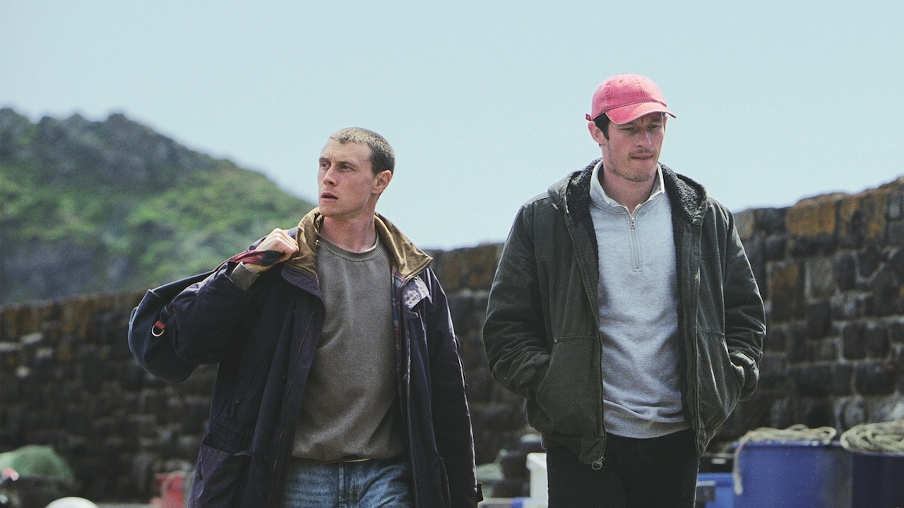 George MacKay as Nick and Callum Turner as Liam walking along a road in Rose of Nevada.