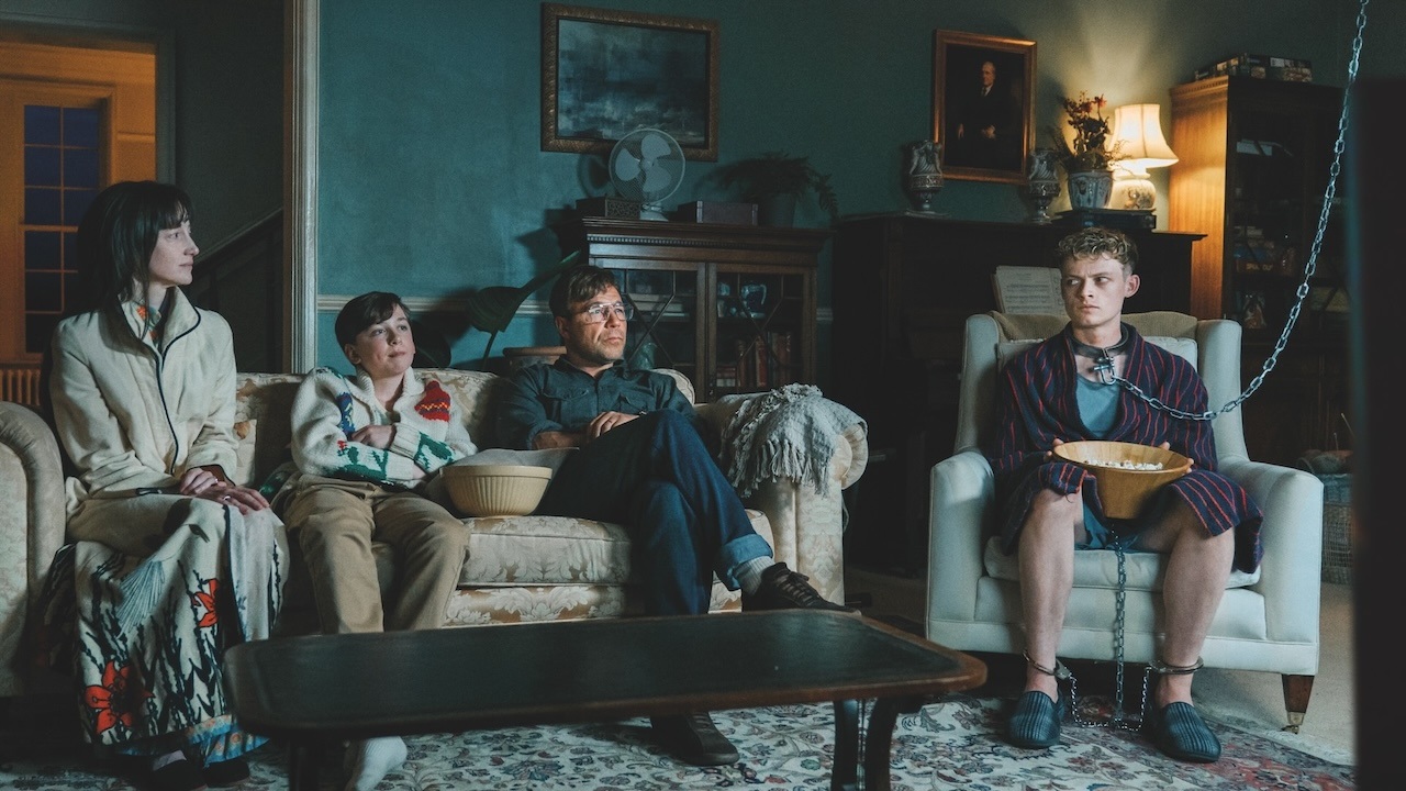 A father. mother and son watch a movie with another man chained up in an armchair next to them in Good Boy.