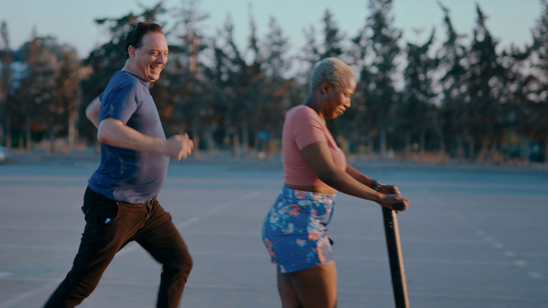 Jolie (Laetitia Ky) riding a scooter with Foued (Foued Zaazaa) running beside in Promised Sky. 